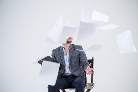 Business man businessman in a suit sitting on a wooden chair and throws documents. On a white...