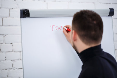 Male speaker businessman manager writes a business promotion plan on a white board. Standing in a black sweater with a marker.の写真素材