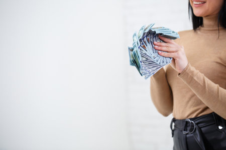 Photo of a charming woman with a smile holding a fan of money in her handsの写真素材