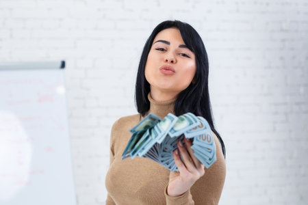 Photo of a charming woman with a smile holding a fan of money in her handsの写真素材