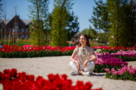 Back view of anonymous woman in summer dress and hat walking near blooming tulips in meadow on sunny day in natureの写真素材