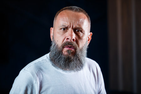 Emotional portrait of an adult gray-haired man with a beard in a white t-shirt