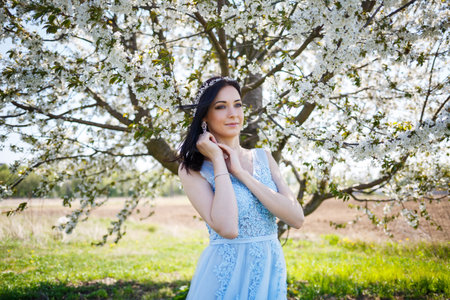 Young woman with beautiful make-up with a vintage hoop in a blue light dress with a bouquet posing on a background of green foliage in a park. Fresh portrait attractive girl with white flowers.の写真素材