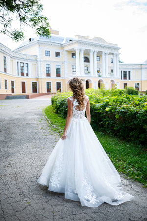 beautiful young girl bride in a white wedding dress with a train walks in the parkの写真素材
