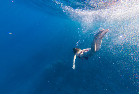 Girl with a mask and a snorkel dives into the sea with corals and fishの写真素材