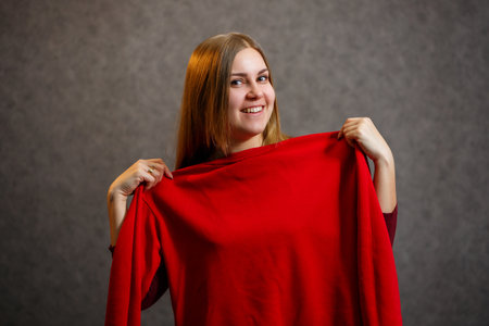 Girl tries on a red sweater on a gray backgroundの写真素材