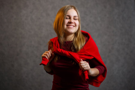 Girl tries on a red sweater on a gray backgroundの写真素材