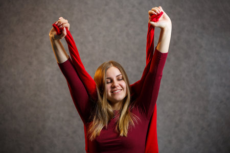 Girl tries on a red sweater on a gray backgroundの写真素材