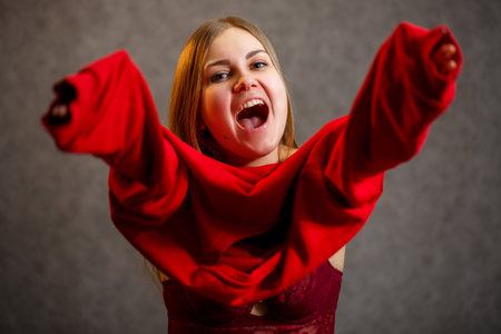 Girl tries on a red sweater on a gray backgroundの写真素材