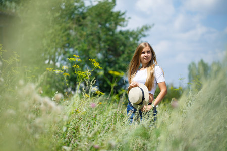 KYIV, UKRAINE - August 2019 young beautiful girl in denim overalls and a light hat walking in the parkの写真素材