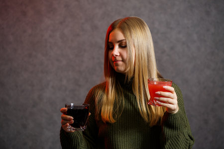 The girl is dressed in a green sweater and holds in her hands glassful with red and black liquid.の写真素材