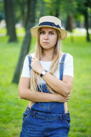 young beautiful girl in denim overalls and a light hat walking in the parkの写真素材