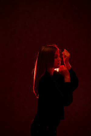 Girl with blond hair emotionally posing on a gray background. Her hair is lit in redの写真素材