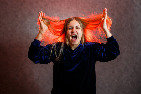 Girl with blond hair emotionally posing on a gray background. Her hair is lit in red