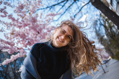 Sakura branches with flowers on a tree on the city streets. Happy woman girl spinning on the street...
