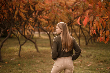 Young beautiful girl dressed in stylish clothes, green sweater and beige pants, in an autumn park with beautiful treesの写真素材