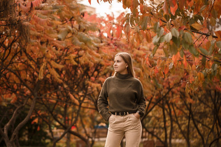 Young beautiful girl dressed in stylish clothes, green sweater and beige pants, in an autumn park with beautiful treesの写真素材