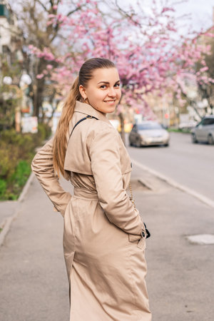 Beautiful woman near sakura trees. Pink flowers bloom in the trees on a city street. Trees bloom around. Spring time conceptの写真素材