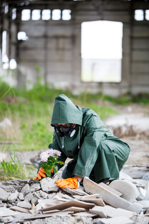 A man in a raincoat and gas mask collects a flower from a scorched, toxic land. Air pollution concept. Ecological catastrophy.の写真素材