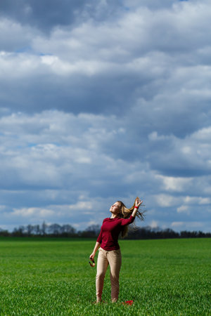 Beautiful young blonde woman stands on green grass in a park. Blue sky with clouds. The girl smiles and enjoys a good day.の写真素材
