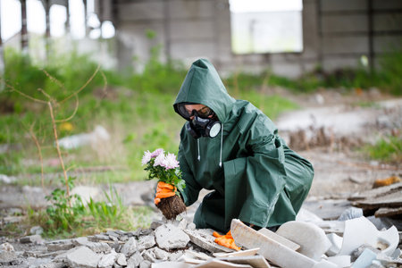 A man in a raincoat and gas mask collects a flower from a scorched, toxic land. Air pollution concept. Ecological catastrophy.の写真素材