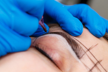 Beautician tattooing a woman's eyebrows using special equipment during permanent make-up, close-up.の写真素材