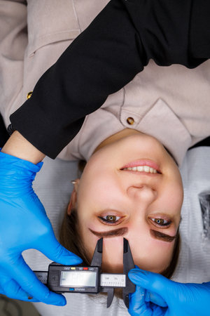 Woman with permanent makeup tattoo on her eyebrows. Close-up beautician makes a sketch of the eyebrows. Professional make-up and cosmetic skin care.の写真素材