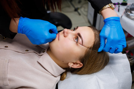Woman with permanent makeup tattoo on her eyebrows. Close-up beautician makes a sketch of the eyebrows. Professional make-up and cosmetic skin care.の写真素材