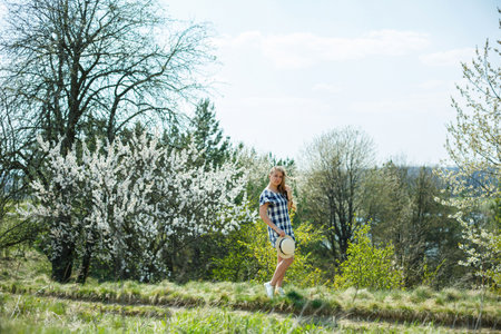 beautiful girl in a dress walking in the spring forest where the trees bloomの写真素材