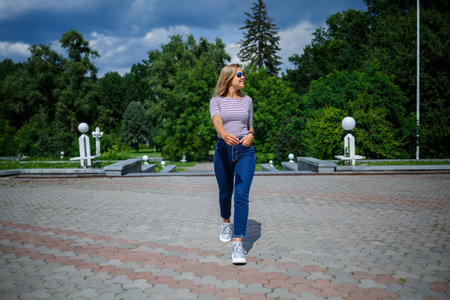 A beautiful girl with blond long hair of European appearance. Dressed in jeans and a T-shirt. Walk on a sunny dayの写真素材