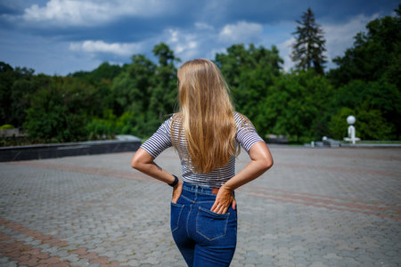 A beautiful girl with blond long hair of European appearance. Dressed in jeans and a T-shirt. Walk...