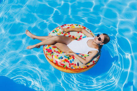 Summer vacation. Tanned woman in glasses in a white swimsuit on an inflatable ring in the poolの写真素材