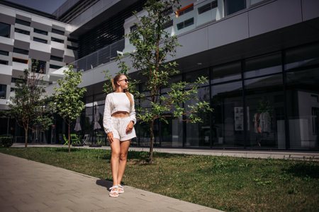 Portrait of young modern businesswoman model. Hot beautiful woman in a white suit posing against the backdrop of the street. Fashionable female walks outdoors in sunglasses.の写真素材