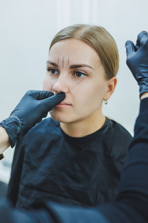 Young woman during professional eyebrow mapping procedure before permanent makeup