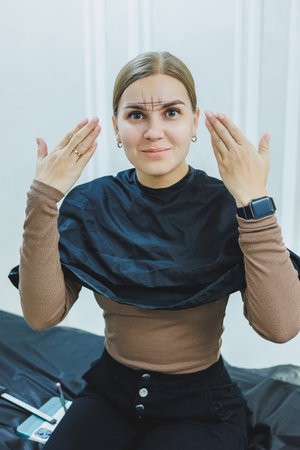 A woman permanent makeup artist draws a sketch of the eyebrows on the face of her client.