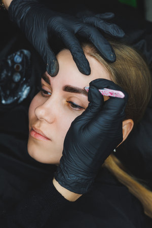 Beautician hand doing brow permanent makeup on an attractive female faceの写真素材