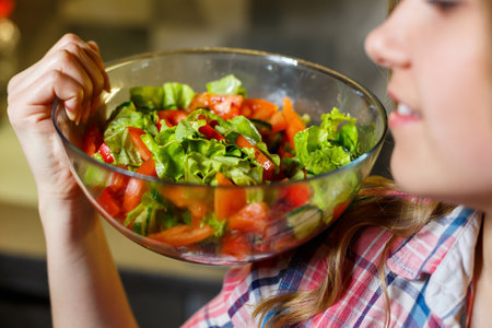 girl fitness trainer vegetarian nutritionist prepare fresh vegetable salad in the kitchen. Watching her figureの写真素材