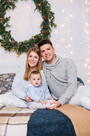 A cheerful young couple with a little son are playing on the bed near the Christmas tree. New Year's...