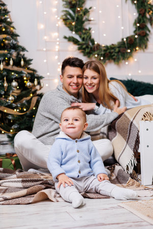 Cute boy with happy parents near the Christmas tree. A family with a small child in a bedroom near a decorated Christmas tree. Festive New Year's atmosphere. Family celebrationの写真素材