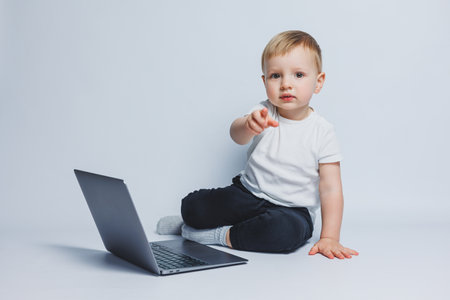A smart boy 3-4 years old sits with a laptop on a white background. A child in a white T-shirt and...
