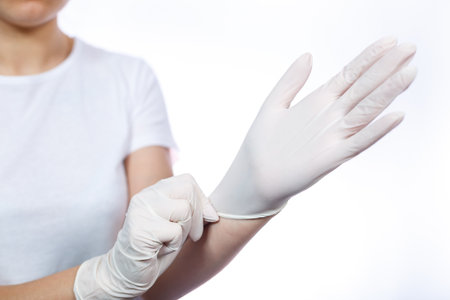 Girl paramedic puts on white medical gloves on hands. Protection against germs and viruses. She is in a white T-shirt on a white background.の写真素材