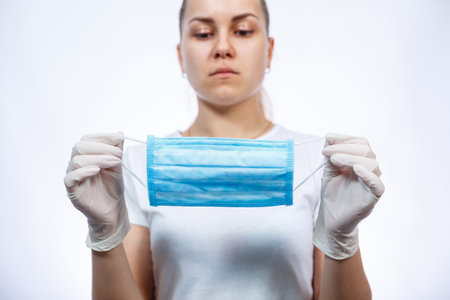 woman health worker demonstrates how to wear a protective medical surgical mask against the virus....