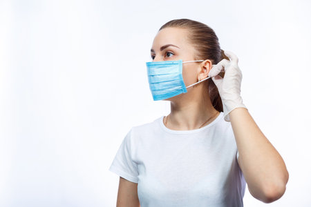 woman health worker demonstrates how to wear a protective medical surgical mask against the virus....