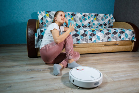 Simple and easy cleaning with modern technology for the household. Girl drinks tea and rests while the vacuum cleaner does the cleaning of the houseの写真素材