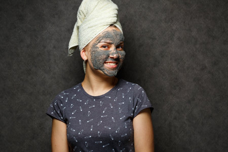 Beautiful young girl with a tonic foam mask on her face and a towel tied with hairの写真素材