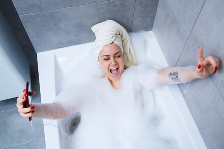 Beautiful young woman listening to music and singing while taking a bath at home. Relax after a hard...