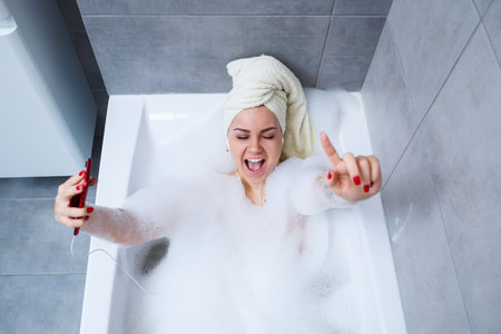 Beautiful young woman listening to music and singing while taking a bath at home. Relax after a hard...