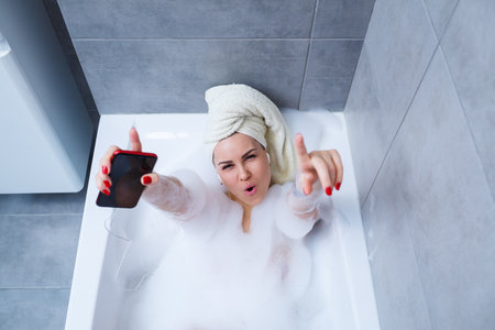 Beautiful young woman listening to music and singing while taking a bath at home. Relax after a hard day. Spa relaxing procedure.の写真素材