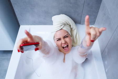 Beautiful young woman listening to music and singing while taking a bath at home. Relax after a hard...