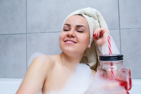 Beautiful young woman with a towel on her head, drinking a cocktail, takes a bath at home. Relax...